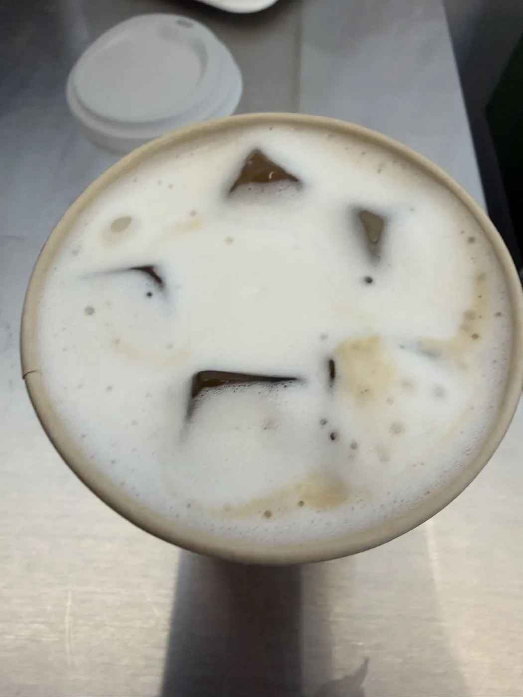 The OG Banana cold brew from above — pale foam over ice in a paper cup, lid on the steel counter