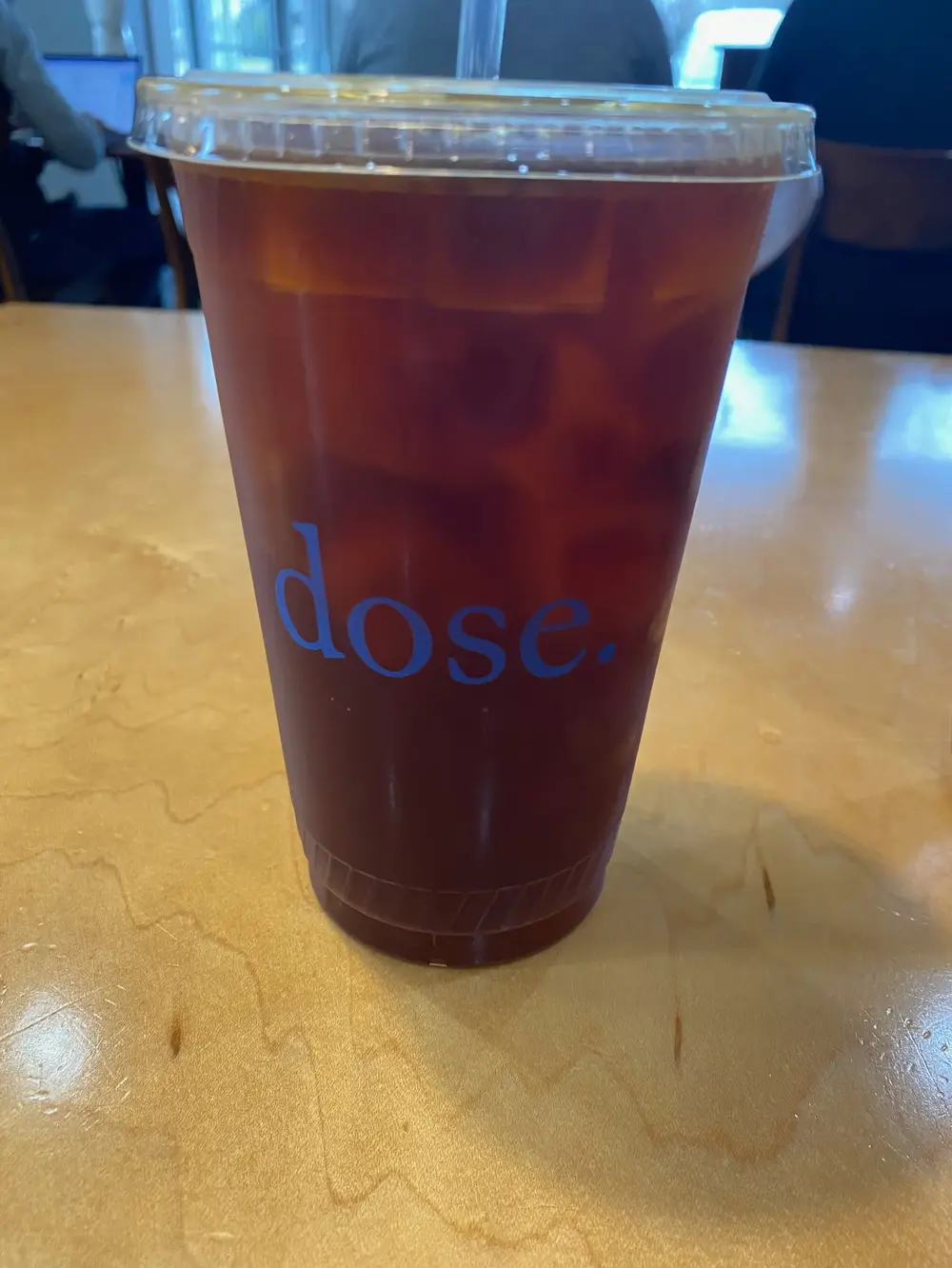 A dose-branded cup of cold brew over ice on a blond wood table in East Nashville