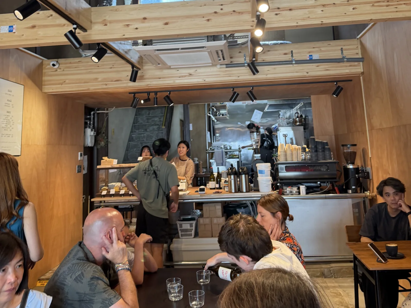Customers gathered around the busy coffee bar beneath exposed wooden beams and track lighting at Nonstop Coffee in Kanazawa