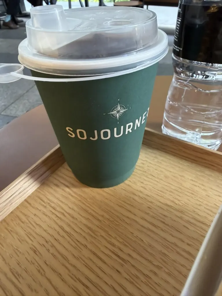 Sojourner's forest-green branded cup on a wooden tray